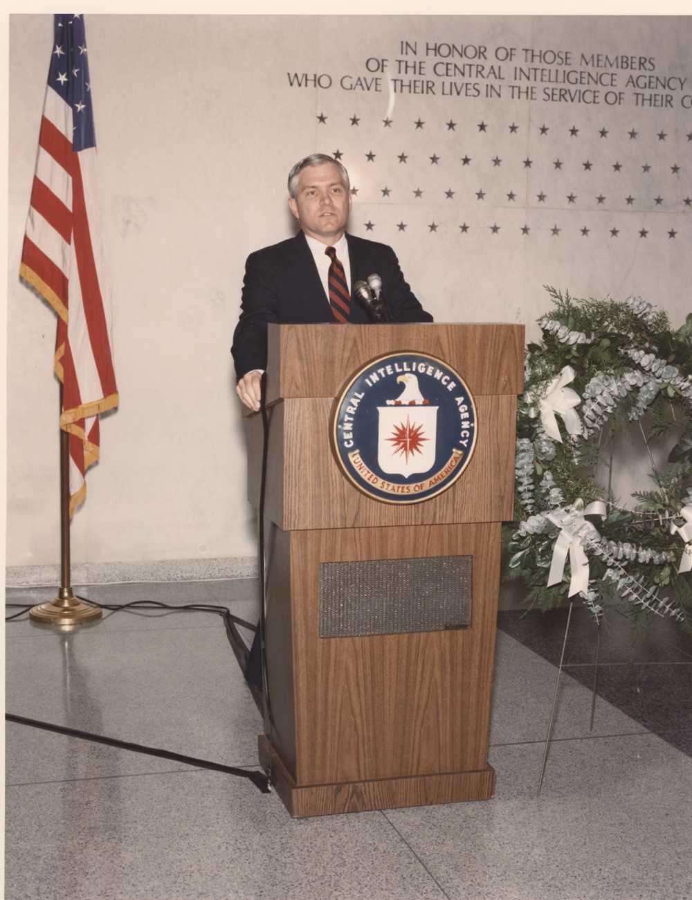 Deputy Director Rober M. Gates speaking behind a podium.